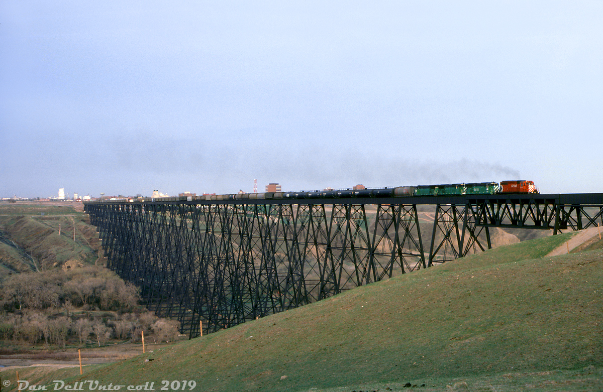 A light plume of exhaust drifts across the Oldman River as CP SD40-2 5614 leads BN B32-8 "B-Boats" 5499, 5498 and 5497 on a freight across the famed Lethbridge Viaduct, a very large steel trestle that was originally built in 1907-1909 (and continues to see freight service today).

The three "BN" B32-8's were actually pre-production GE Test bed/demo units built in 1984 that were just painted for Burlington Northern. They demonstrated on CP in 1985, but inevitably produced no orders for these high-horsepower 4-motor units (CP had just finished bulking up on 6-axle GMD SD40-2 units for mainline service, and was still taking delivery of scads of 4-motor GP38-2's for prairie branchline service at the time). After their demo stint they were leased by BN until being returned to owner GE in 1991. Research suggests unit 5497 was scrapped in the mid-90's, and 5498/99 lingered in a derelict state at GE in Erie PA until the early 2010's. In the end, the only roads to opt for the B32-8 model were Norfolk Southern and Amtrak.

Doug Wingfield photo, Dan Dell'Unto collection slide (with some colour correction/editing).