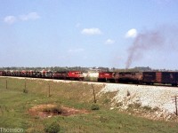 Two Canadian Pacific freights meet at Coakley, east of Woodstock around Mile 86 of CP's Galt Sub. An MLW C424 and RS18 lead a westbound with some open autoracks full of new automobiles on the head-end, while the other freight is an eastbound with a pair of back-to-back RS18's in charge. The old CP maroon and grey "script" livery was still prominent on the railway in the early 70's, just a few years after CP introduced their new "CP Rail" livery and branding.