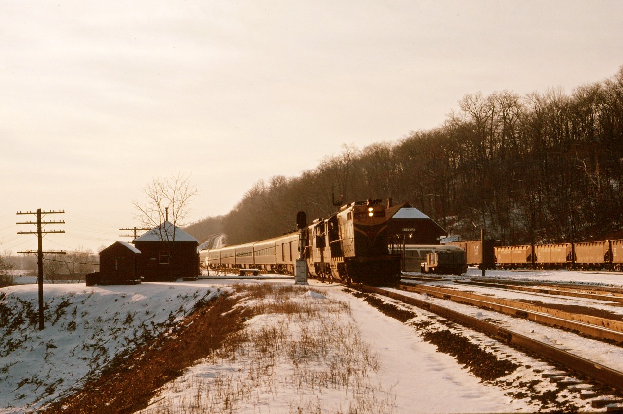 Train No. 6, the "Inter-City Limited" from Chicago, makes its stop at Dundas in January 1963. In the background, you can see the connecting bus for Hamilton waiting next to the station (which is an active train order office), as well as hopper cars for Canada Crushed Stone--just to the east of this location. Also note the colour light block signal and maintenance of way buildings to the left of the train.
