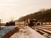 Train No. 6, the "Inter-City Limited" from Chicago, makes its stop at Dundas in January 1963. In the background, you can see the connecting bus for Hamilton waiting next to the station (which is an active train order office), as well as hopper cars for Canada Crushed Stone--just to the east of this location. Also note the colour light block signal and maintenance of way buildings to the left of the train. 