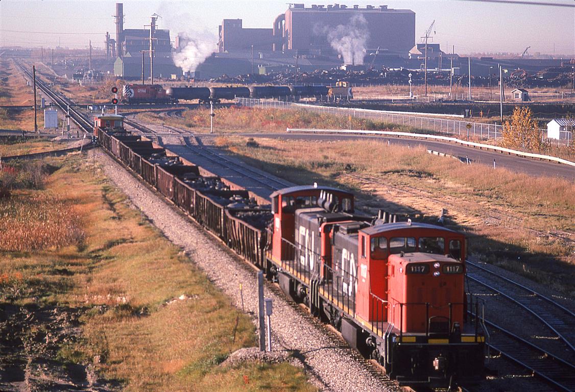 This photo is in response to Larry Parks contemporary shot of the area. With all the vegetation now here, the track layout is more difficult to make out.
The CN work extra is stopped at the CP crossing as a local passes eastbound.
Stelco (?) owns that huge facility.