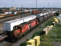 A yard job, or perhaps a local, has a string of 5 grain hoppers in tow, while a container train can be seen in the background.