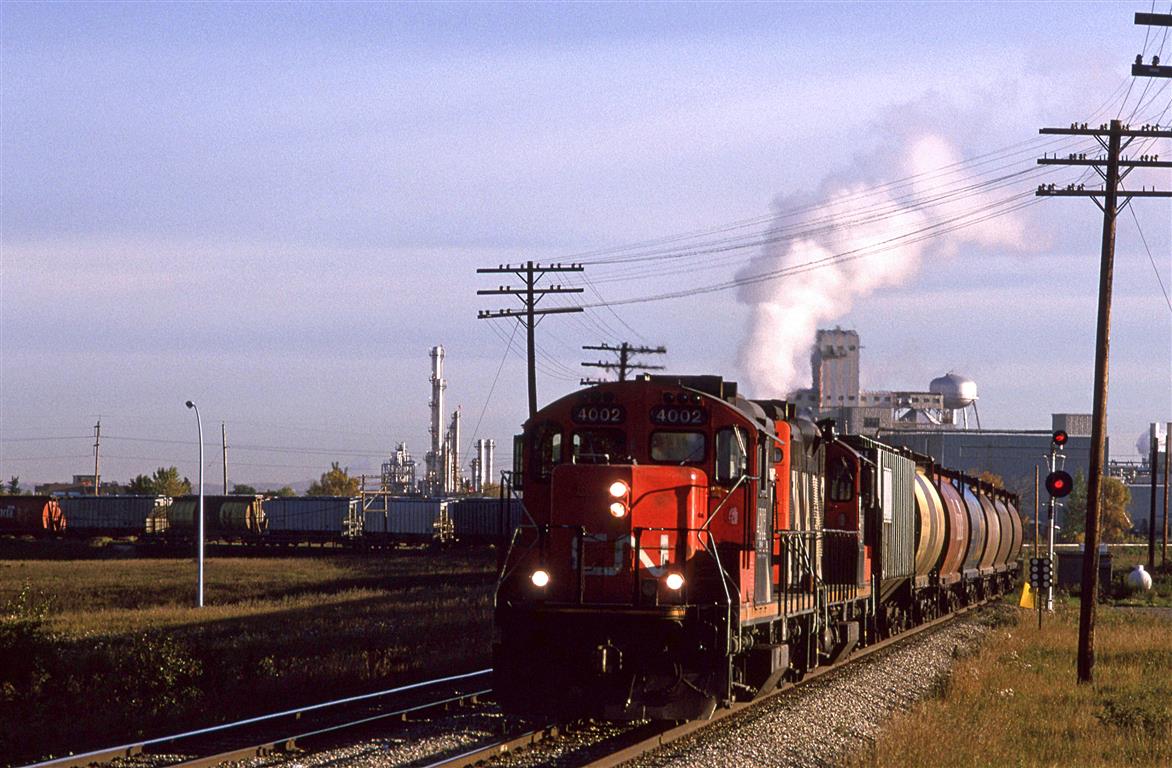 Train 520, the Camrose turn, has just left the Wainwright Sub, and is now headed south on the Carmose Sub. In tow, it a lengthy string of grain hoppers,
The steam is coming from a Celenese chemical plant,that has since disappeared.