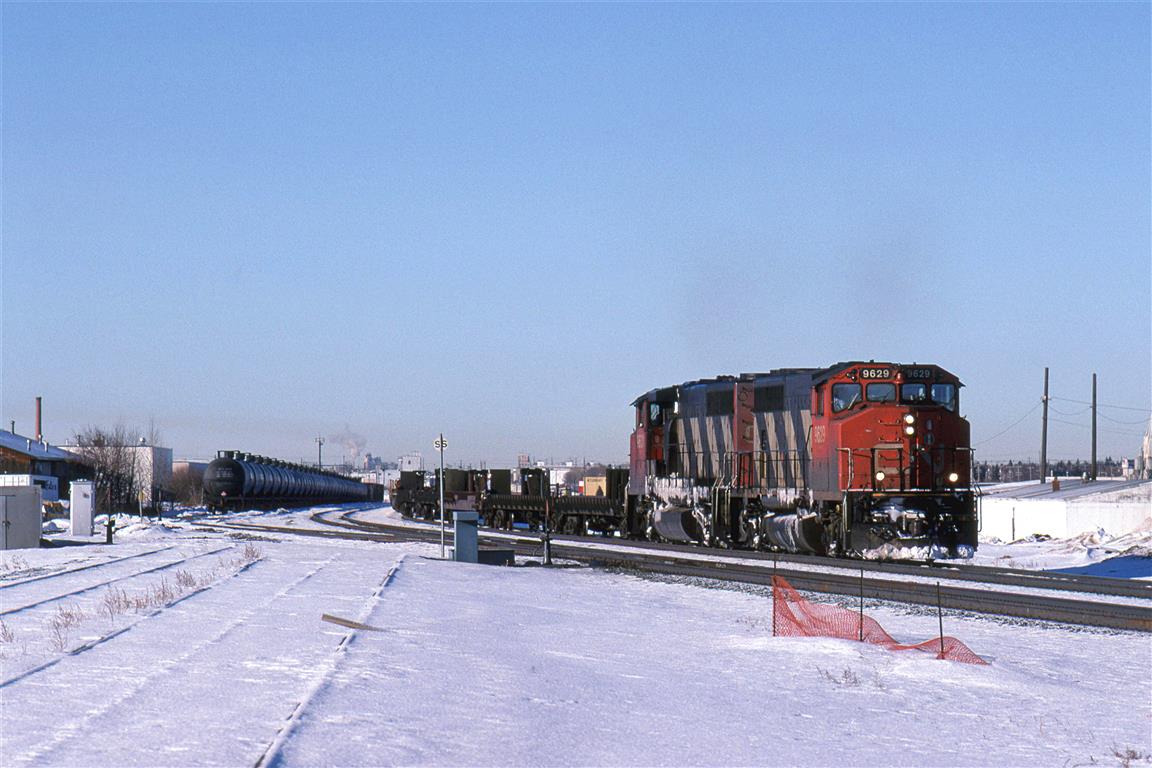 This temporary curve is a shoe-fly track put in to allow for the construction of the 50th St underpass.
The proper alignment may be seen at left.
I do not know why the string of tanks cars are parked here. Storage? Set out for pickup by a specific train?
122 will have nothing to do with the tank cars. It is a priority COFC train.