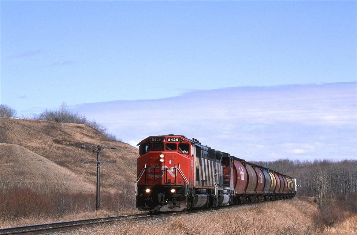 This is another area that I found by studying topo maps. The Camrose Sub winds down this valley from the town of Camrose to cross the Battle River Valley. My hopes were that I could obtain a view looking up this small valley from the south rim of the Battle River Valley. Trees and houses precluded that plan. I always wanted to explore this small valley for photo opportunities. I will manage to see the upper end but I was not able to really get to know the bottom  area. There are several wooden trestles in this small valley.
Ferlow Junction, in the Battle River Valley is where a branch splits off the Camrose sub. The branch, whose name escapes me, went to Stettler and may have been spun off to a tourist line at this time.
As for the train, it is an Edmonton to Calgary grain Empty. Presumably, cars were dropped at elevators on the way to Calgary, and picked up on the way back north