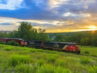 Nearing sunset, the sun dips below the clouds just enough to light up the sky and scene, as train 406 heads along the countryside, at Norton, New Brunswick.