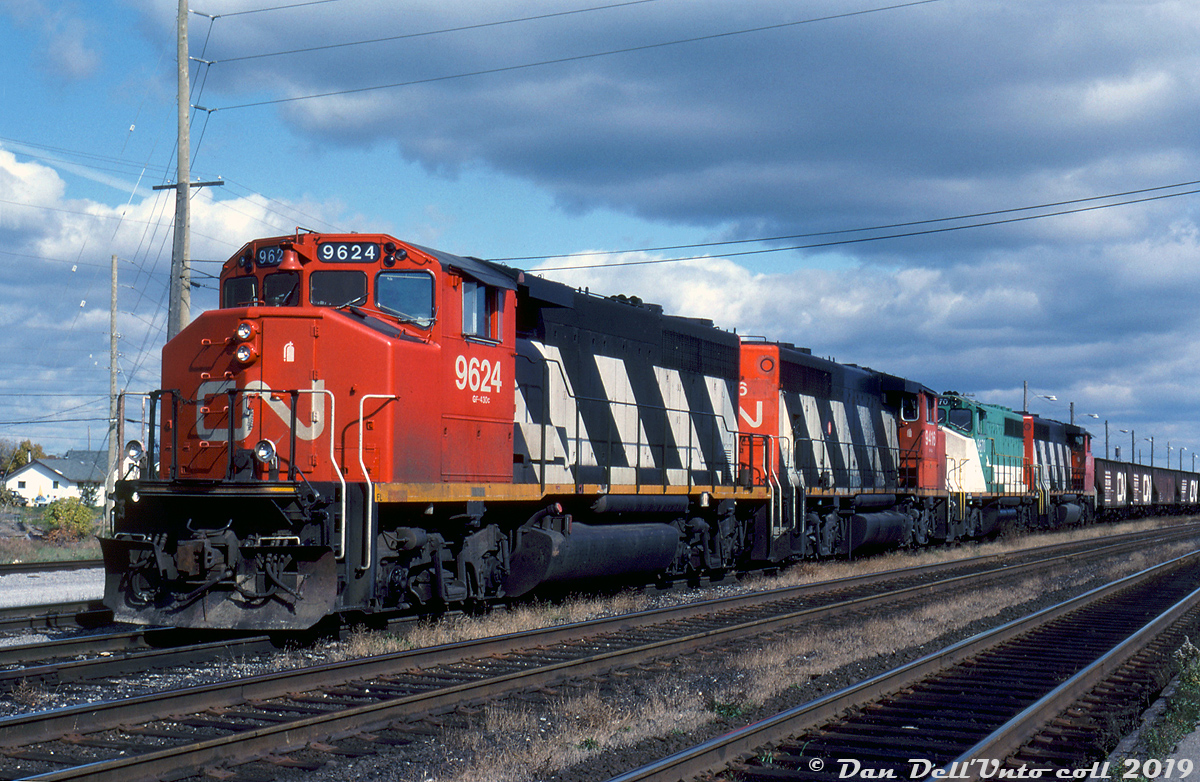 Duck, Duck...Goose! A CN freight sits near VIA's Belleville Station on CN's Kingston Sub, awaiting departure westward. Four of CN's unique GMD-built Canadian Safety Cab-equipped GP40-2 units are in charge today: matching zebra-striped GP40-2L(W) units 9624, 9416, and third sister unit, plus newly acquired GP40-2(W) 9670 still bearing her former owner GO Transit's colours.

CN and GO Transit were the only two roads to order the safety cab-equipped GP40-2 model, and GO sold 10 of their 11 commuter-service units off to CN around summer or fall 1991 after enough F59PH's were around to render some of GO's older power surplus. They had the GO markings removed but were put into freight service in their old GO colours with new CN numbers 9668-9677, numbered above CN's last order of units. From cross-referencing other photos, the units only ran like that for a year or so, as most appear to have visited the paint shop during 1992 for their zebra stripes.

Ron Visockis photo, Dan Dell'Unto collection slide.