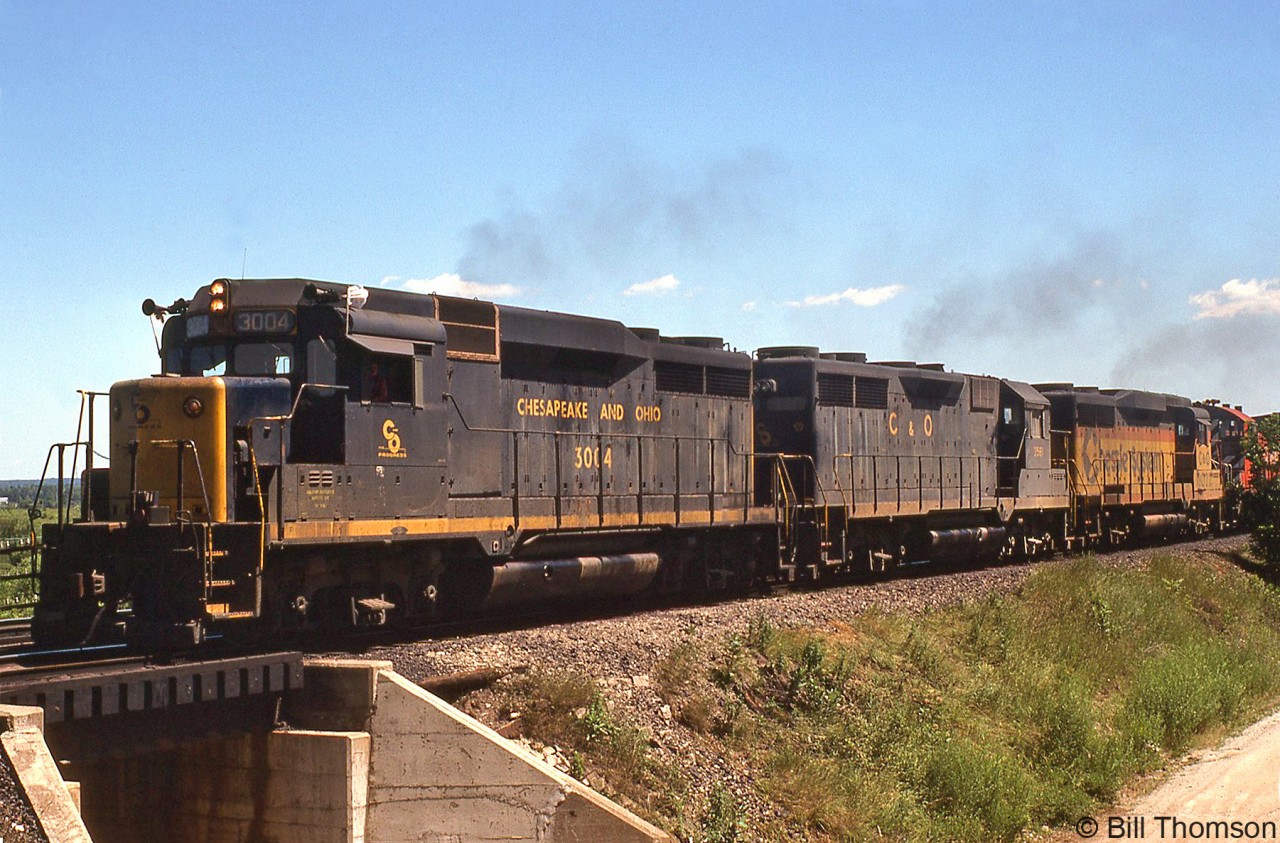 Working hard with extra flags flapping and no shortage of exhaust, Chesapeake & Ohio GP30 3004, GP35 3561, GP30 3022 and a CP 8100-series SW1200RS climb the grade at Kelso near the former location of CP "Christie" (Mile 35.8 to the west, removed from timetables sometime in the early 70's), heading a westbound CP freight on the Galt Sub on a sunny July day in 1979.  Power-short CP commonly borrowed C&O (and B&O) power at the time, typically GP30's, GP35's, GP38's and GP40's that were painted in the older blue/yellow or the newer Chessie paint.More CP action around Christie/Kelso:Steam-era climbing the hill: http://www.railpictures.ca/?attachment_id=28855Leased B&LE power: http://www.railpictures.ca/?attachment_id=17031F-units by the Kelso ski hill: http://www.railpictures.ca/?attachment_id=17335