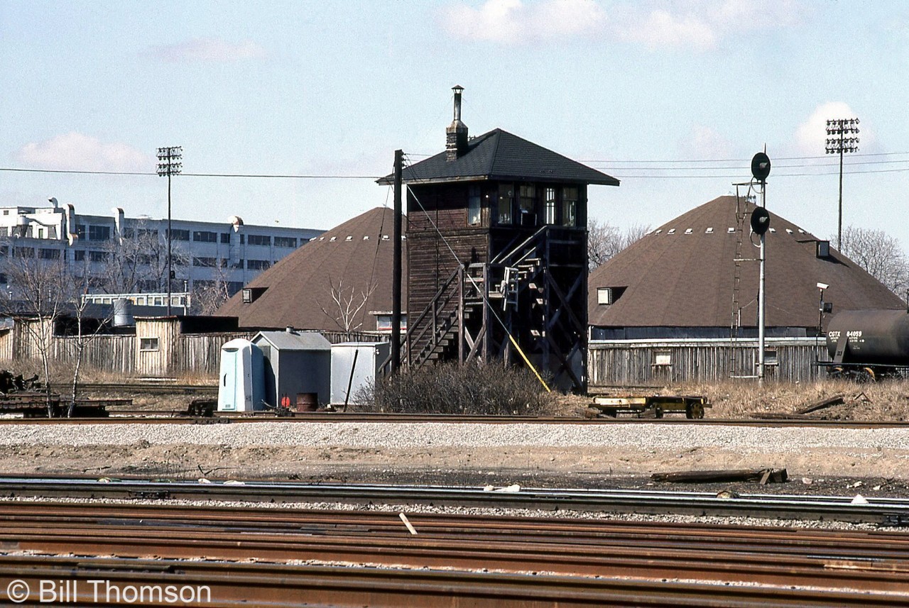CPR's Tecumseh Street interlocking tower is pictured at Mile 1.3 of CP's Galt Sub, as seen looking north from CN's Oakville Sub just west of Cabin D & Bathurst Street.  One of the more obscure and less well-known interlocking towers in the downtown Toronto area, Tecumseh Street tower could be found under the "Toronto Terminals Division" section of CP timetables at Mile 1.3 CP Galt Sub, and also noted under the CP Galt Sub instructions for Parkdale Yard. It was located a stone's throw from Cabin D between Strachan Ave. and Bathurst St. (named after the nearby Tecumseh St.) and staffed and operated by CP mainly to control a CP track that headed southeast from Parkdale Yard and crossed's CN Weston Sub at the Tecumseh Street interlocking (just west of Bathurst St./Cabin D) to access the King Street Shed Lead on the north side that ran up to CP's freight sheds in the King/Simcoe St. area. Ray Kennedy's Old Time Trains page has a photo of the interlocking diamonds here.  The tower was removed by 1985, around the time when the Bathurst St./Cabin D interlocking area was starting to be modernized and automated (much of the old plant in this area used to be manual switches operated by switchtenders on the ground).  The two sand domes belong to the City of Toronto on their property near the old Wellington destructor. The tank car on the far right is spotted at one of the Toronto Abattoir/Quality Meat Packers sidings.