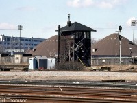 CPR's Tecumseh Street interlocking tower is pictured at Mile 1.3 of CP's Galt Sub, as seen looking north from CN's Oakville Sub just west of Cabin D & Bathurst Street. <br><br> One of the more obscure and less well-known interlocking towers in the downtown Toronto area, Tecumseh Street tower could be found under the "Toronto Terminals Division" section of CP timetables at Mile 1.3 CP Galt Sub, and also noted under the CP Galt Sub instructions for Parkdale Yard. It was located a stone's throw from Cabin D between Strachan Ave. and Bathurst St. (named after the nearby Tecumseh St.) and staffed and operated by CP mainly to control a CP track that headed southeast from Parkdale Yard and crossed's CN Weston Sub at the Tecumseh Street interlocking (just west of Bathurst St./Cabin D) to access the King Street Shed Lead on the north side that ran up to CP's freight sheds in the King/Simcoe St. area. Ray Kennedy's Old Time Trains page has a photo of the interlocking diamonds <a href=http://www.trainweb.org/oldtimetrains/CPR_Toronto/PARKDALE.htm><b>here</b></a>. <br><br> The tower was removed sometime later in 1984, around the time when Cabin D was removed and the Bathurst St. interlocking area was starting to get modernized and automated (much of the old plant in this area used to be manual switches operated by switchtenders on the ground). <br><br> The two sand domes belong to the City of Toronto on their property near the old Wellington destructor. The tank car on the far right is spotted at one of the Toronto Abattoir/Quality Meat Packers sidings.