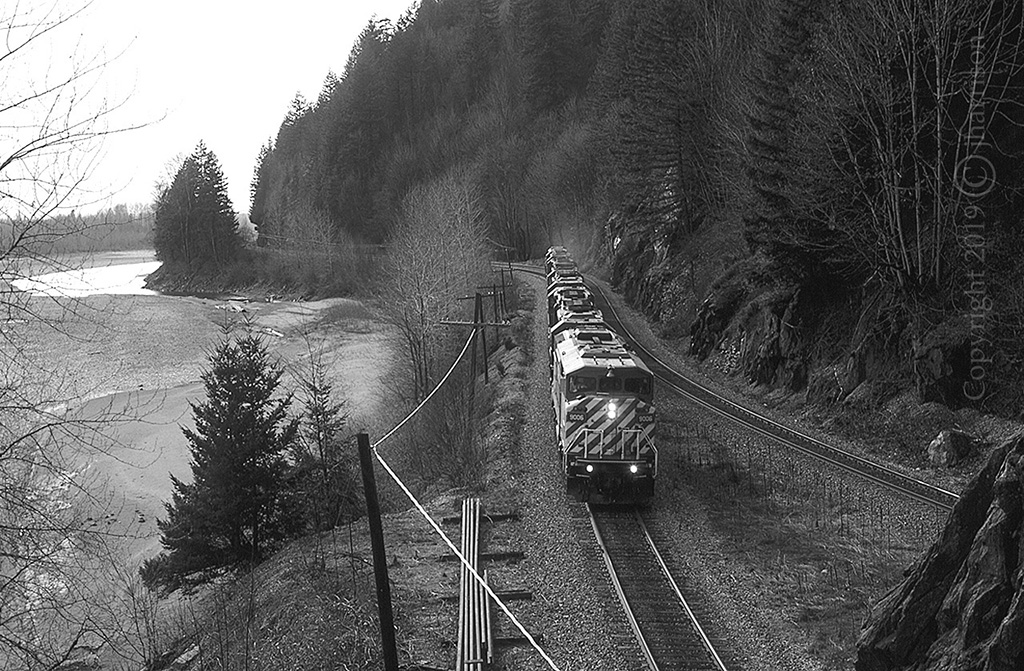 An eastbound CP power transfer about to enter the east track portal at Harrison Mills on CP's Cascade Sub. The lead unit is the 9006 with trailing units 5974 / 5962 / 5997 / SOO 6025 / CP 6071 / 5761 and 5525. From what I can gather, only the SOO 6025 remains in service. It was renumbered to CP 6225 in 2011. Station name signs have changed over the years. In 1995 this location was known as Harrison Mills. No relation.