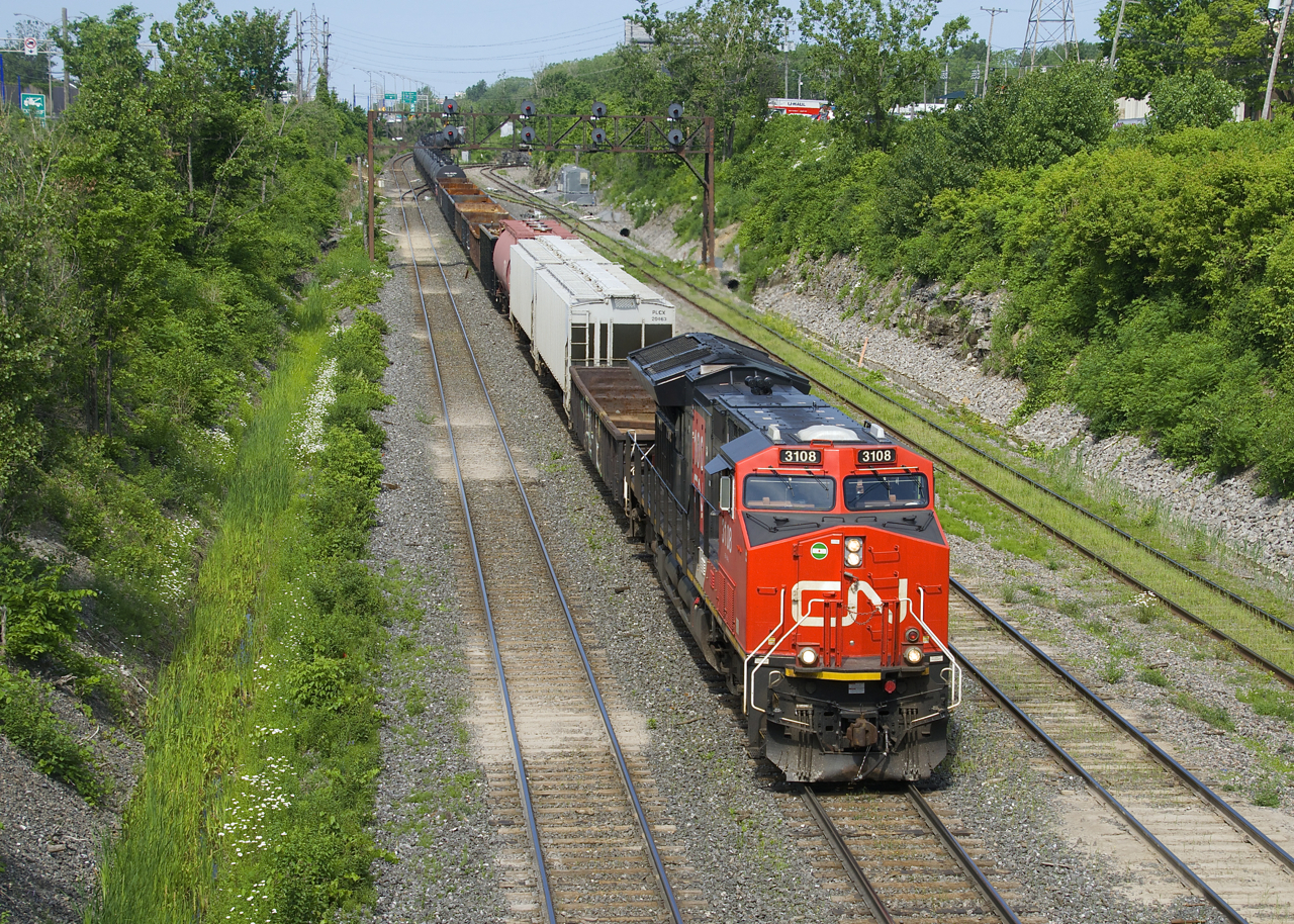 A 167-car CN 310 has CN 3108 up front (with a slapdash 'CN 100' logo addded on the long hood) and CN 3089 mid-train as it passes underneath a signal gantry.