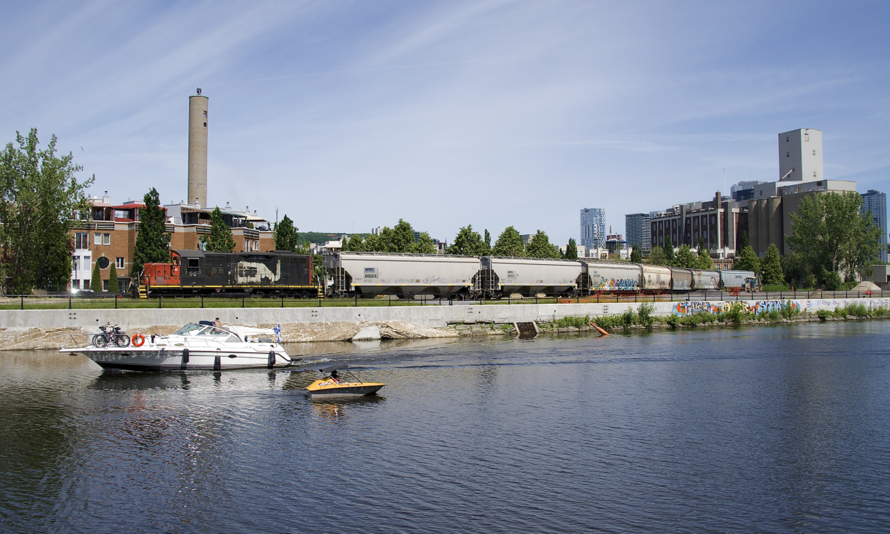 It's a holiday in Quebec (Saint-Jean-Baptiste Day) and the boaters are out in full force on the Lachine Canal as two boats pass CN 7229 and 7 grain loads, heading towards the Ardent mill (seen at far right).