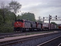 A CN freight powered by HR616, M636, and SD40 is eastbound on the south track through CN Aldershot West, a year or so after the Aldershot Yard expansion moved its west-end connection here. <br>Cars on the train include an orange and white Dupont Canada "sclair" covered hopper, 5 well-car platforms ahead of it, and a head-end flat car carrying highway trailer SPLZ 731342 with "Southern Pacific Golden Pig Service" - emblem is a smiling pig wearing an SP cap. <br><br>Vantage point is the wrong side of the tracks from a public access point of view, times have changed. The chimney of the former Burlington Brick works, beyond Lemonville Road bridge, is further away than it looks.