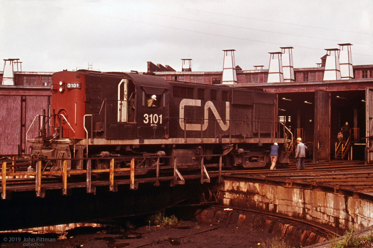 CN 3101 gets some attention from maintenance staff at the Fairview roundhouse in Halifax. 
The gentleman with a blue jacket is likely inspecting or working on some part of the truck - as there are better places for pushing an RS-18, and you'd need a lot more people.
Fairview roundhouse was demolished in 1991.
