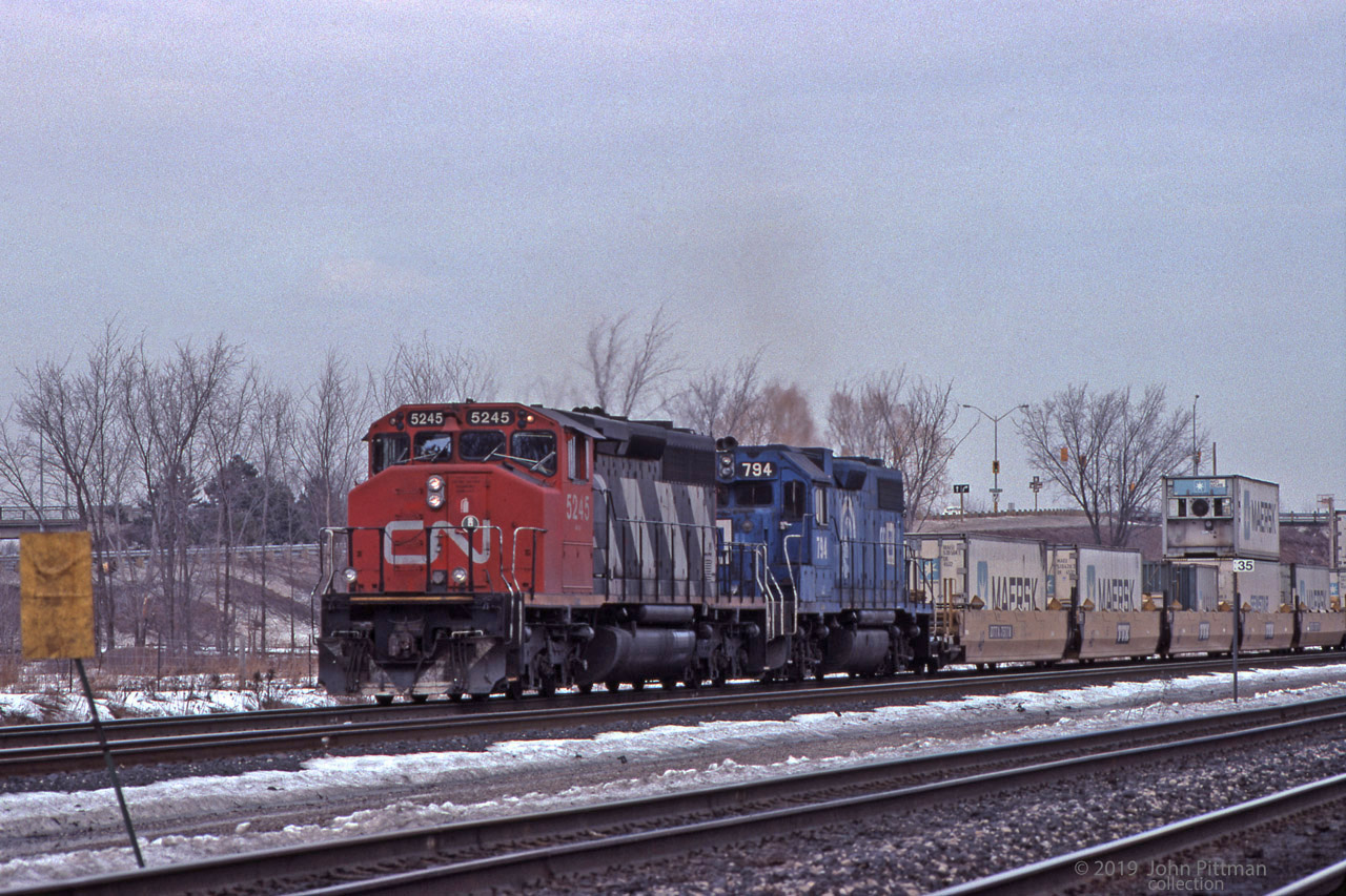 A CN SD40-2W and an ex-Conrail EMDX GP38-2 power a westbound train at the west end of Aldershot Yard, beside Milepost 35. Well cars carrying intermodal containers are at the head end; 6 Maersk and a Genstar are visible. Very probably the train entered Aldershot Yard to drop and/or lift railcars.
CN rented a number of EMDX units in this timeframe.
EMDX 794 is probably ex-CR 7994, previously PC 7994. EMDX sold off their ex-CR GP38-2's to various companies; some are currently owned by GATX (GMTX) so it's possible some are back on CN.
Just hearsay, but I read that EMD entered the 2nd-hand locomotive rental business because Conrail balked at paying EMD's buyout price for their fleet of ex-PC GP38-2's when its lease ended. It was said that Conrail tended to favour GE thereafter.