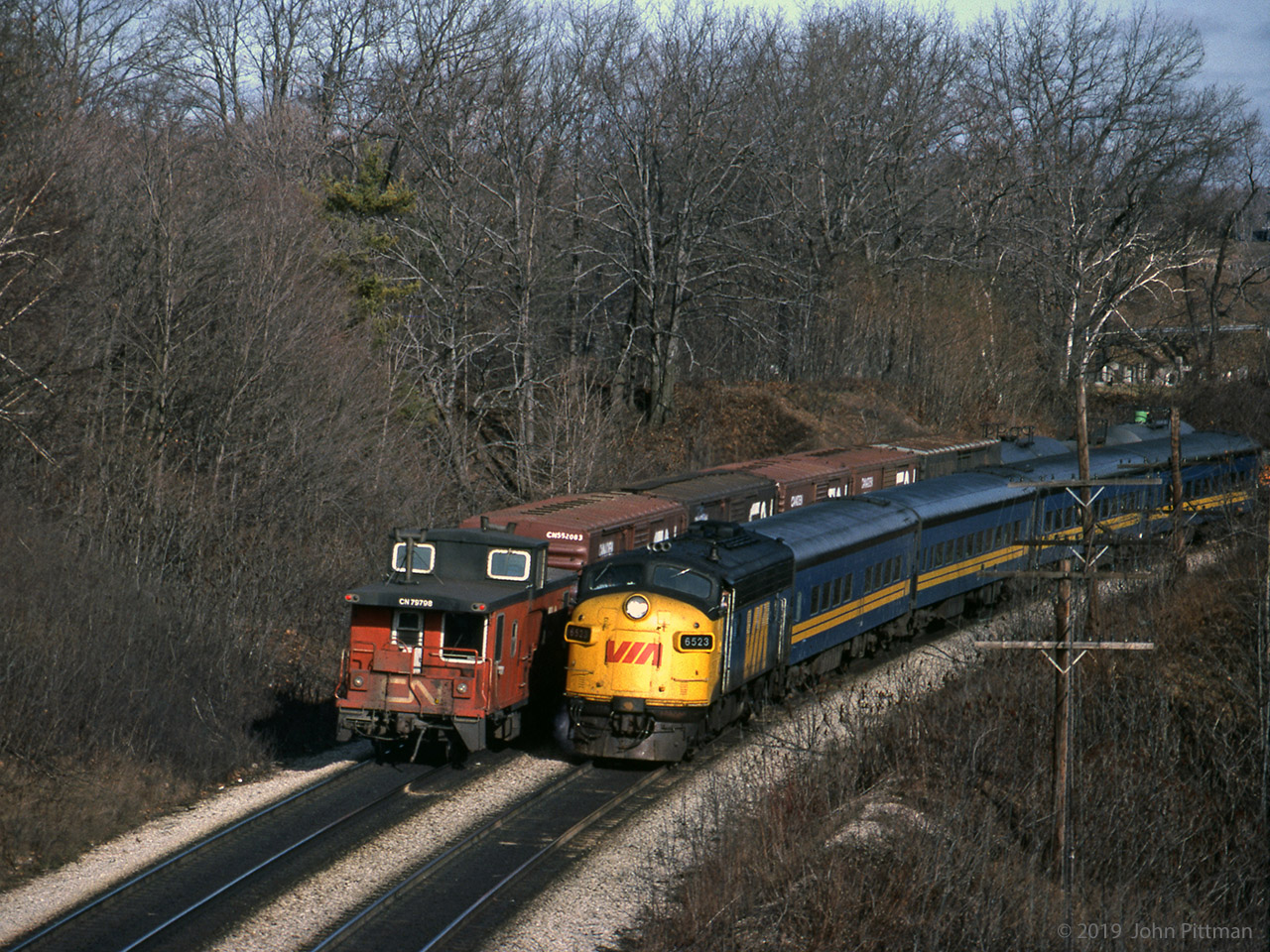 GMD FP9A VIA 6523 leads its train of 4 blue coaches timetable-west on the Oakville Sub south track, approaching CN Bayview (Jct), as seen from Plains Road "Wolfe Island bridge".
It is almost past an eastbound CN freight train on the north track with caboose CN 79798 at the end.
Date written on slide matches Kodachrome Jan 83 process date.