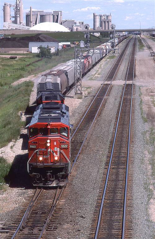 Just another Edmonton to Vancouver grain train departing town.
Inland Cement dominates the background, but there is an asphalt plant just this side of Inland. Apart from trees growing along the RR ROW, and a landfill mountain, this view has is pretty much the same today.