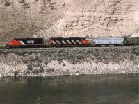 A westbound CN grain train passes by an interesting slope. Grazing animals created the converging line on the hill at left, while rivers and lakes created the interesting bedding in the poorly consolidated "rock" formation at right.