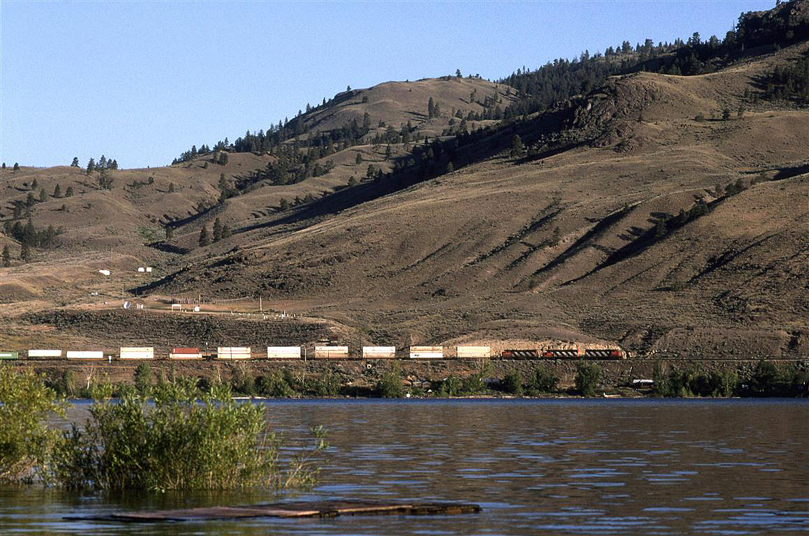 From the town of Savona, looking across Kamloops Lake, this eastbound double stack train quietly glides by on the flat, but twisted track along the north side of the lake.