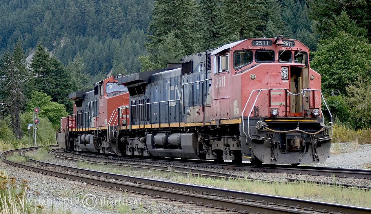 CN 2511 with the 2620 trailing are westbound, and stopped at Boston Bar East, awaiting a crew change before switching over to CN's Yale Sub. Chaumox Road crosses the tracks here and leads down an embankment, where it crosses the Fraser River, and into the village North Bend and CP's North Bend yard.