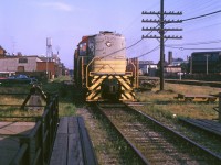 On a sunny summer evening, CP S2 7026 works on the "Old Bruce" service track in the West Toronto Junction area, switching a few industries located along the east side of the rail corridor at Bloor Street West underpass. 7026 was one of the <a href=http://www.railpictures.ca/?attachment_id=35550><b>longtime Toronto-assigned</b></a> Alco switchers that took care of local and yard switching duties for decades, at the time assigned out of Lambton Yard. A CP RS18 is visible in the background on CP's Galt Sub, which was separated from the old Bruce service track by CN's Weston Sub that ran through the middle of the corridor. Judging from some other slides taken at the same spot at the same time, the unknown photographer (likely visiting from the US) was taking photos of TTC streetcars on Bloor off the top of the bridge, and probably snapped a shot of this switching job when it showed up. <br><br> This industrial spur was originally part of the Toronto, Grey and Bruce's mainline from Toronto to Orangeville. While the TG&B line north of the diamond became CP's MacTier Subdivision, this section south of the diamond became a CP service track to serve the local industries along Perth Ave. and Sterling Rd. between the diamond and Dundas Street (overpass visible in the distance). Those included Viceroy Rubber at Dupont, Solway & Sons, Glidden paints, Aluminum Goods Ltd (Alcan), Scythes & Co., and Rowntree Co. Ltd (chocolates, later Laura Secord, today Neslie's Sterling Rd. plant). There were also CN-CP interchange tracks south of Dupont, between the service track and CN's Weston Sub. According to Ray Kennedy's <a href=http://www.trainweb.org/oldtimetrains/OandQ/TGandB/history_tgb.htm><b>Old Time Trains site</b></a> and track diagrams, the service track ended by entering Compressed Metals' scrapyard south of Dundas and coming out the other side as a CN siding north of Parkdale. The old Bruce service track was abandoned and removed in the 90's (after Laura Secord, who received sugar from Redpath downtown, switched to trucks). In more recent years the right-of-way has been turned into the West Toronto Railpath after lying abandoned until the late 2000's. The old track bumper on the right by Milnes Coal & Fuel just south of Bloor remained intact in the weeds until construction began. <br><br> <i>Photographer unknown, Dan Dell'Unto collection slide.</i>