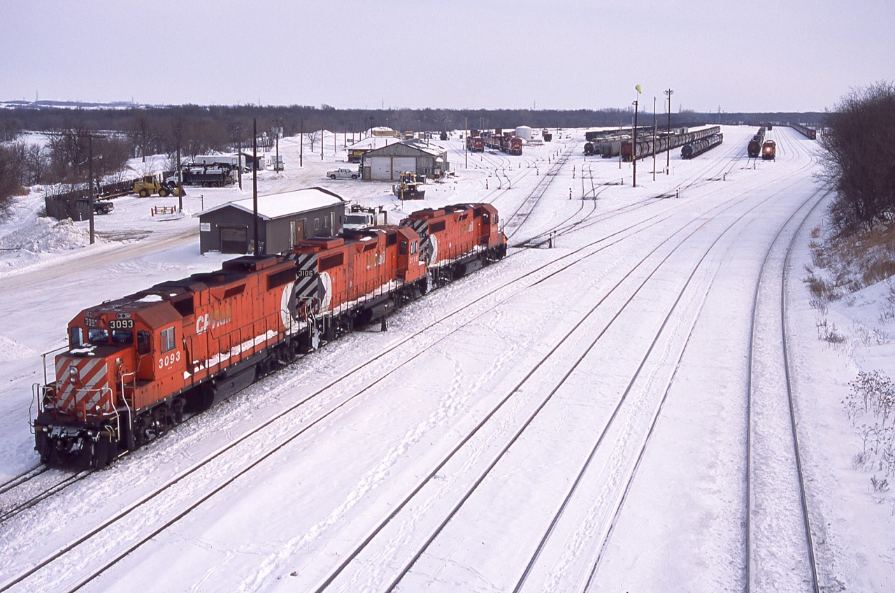 Its that time of year again, where winter photos look comfortable compared to the summer heat.  

It's a busy morning in Brandon as two sets of GP38's are seen switching the west end of the yard. In the distance a westbound grain train pulls down the main towards the station for a crew change.