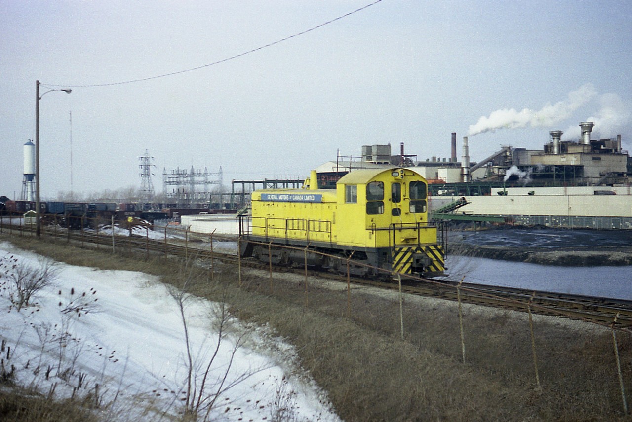 The yellow General Motors of Canada switcher was a hard one to catch, and back then it certainly was busy, usually deep in the depths of endless boxcars and such. I remember the unit bearing the number 47174, but someone please correct me if possible.
Note GMs own water supply....looks from this angle almost like a moat. As for location; behind the freight cars is the Welland Canal, east side, the switcher is actually in Thorold and the GM plant is in St. Catharines.
I have no information on the switcher's status or anything else about what transpires back behind the GM these days.  Perhaps one of the locals who contributes to RP can fill us in!!
I am standing just off on the north side of the CN Grimsby sub.