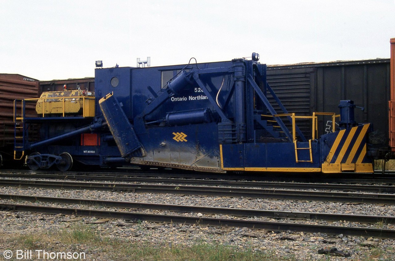 Ontario Northland 528, a Jordan spreader, is pictured stored at Cochrane between two boxcars. According to the Canadian Trackside Guide, it was built by the O.F. Jordan Company in 1945 as a Type A spreader, serial number 795. Jordan spreaders are handy for both plowing sidings and yards during the snowier seasons, and spreading ballast and cutting ditches during the warmer months.