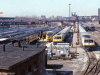 VIA's (formerly CN) Spadina Coachyard in Downtown Toronto is pictured in March of 1984. The tracks are teaming with passenger equipment, including VIA LRC consists with locomotives 6916 and 6921, an Ontario Northland TEE train for the Northlander, Tempo cars, cars from the blue and yellow fleet, a steam generator car, and old heavyweights including some baggage cars still painted in CN colours. All of this was switched by a fleet of <a href=http://www.railpictures.ca/?attachment_id=27375><b>CN S13 units</b></a>, five of which are visible. They also <a href=http://www.railpictures.ca/?attachment_id=30123><b>shuttled entire consists</b></a> to and from nearby Union Station.
<br><br>
By this time in the mid-80's all of the former CN steam-era facilities and yards at Spadina were on borrowed time. Soon VIA would move operations to nearby Mimico (the new Toronto Maintenance Centre and yards), and the downtown railway lands would be cleared in preparation for construction of the new Skydome (Rogers Centre) where the old Spadina roundhouse was. Most of the former coachyard property would lay empty until development years later, into mostly condos.