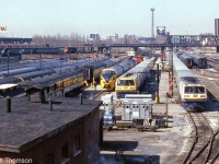 VIA's (formerly CN) Spadina Coachyard in Downtown Toronto is pictured in March of 1984. The tracks are teaming with passenger equipment, including VIA LRC consists with locomotives 6916 and 6921, an Ontario Northland TEE train for the Northlander, Tempo cars, cars from the blue and yellow fleet, a steam generator car, and old heavyweights including some baggage cars still painted in CN colours. All of this was switched by a fleet of <a href=http://www.railpictures.ca/?attachment_id=27375><b>CN S13 units</b></a>, five of which are visible. They also <a href=http://www.railpictures.ca/?attachment_id=30123><b>shuttled entire consists</b></a> to and from nearby Union Station.
<br><br>
By this time in the mid-80's all of the former CN steam-era facilities and yards at Spadina were on borrowed time. Soon VIA would move operations to nearby Mimico (the new Toronto Maintenance Centre and yards), and the downtown railway lands would be cleared in preparation for construction of the new Skydome (Rogers Centre) where the old Spadina roundhouse was. Most of the former coachyard property would lay empty until development years later, into mostly condos.