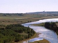 A westboind intermodal train comes out of Calgary along the Bow River at the westernmost end of Bearpaw Reservoir. Calgary Olympic Park facilities and urban sprawl can be seen on the horizon