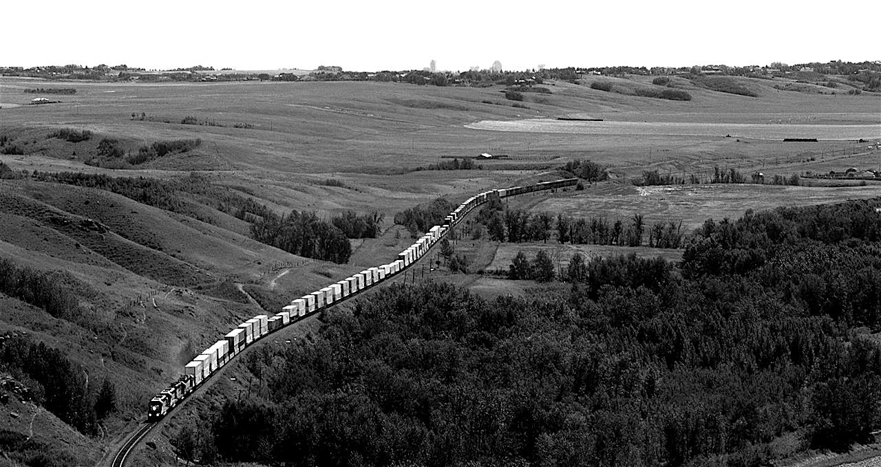 Downtown Calgary peeks over the hill forming the north side of Bow Valley, west of town. An intermodal snakes through some of the prettiest country this close to a major urban area.