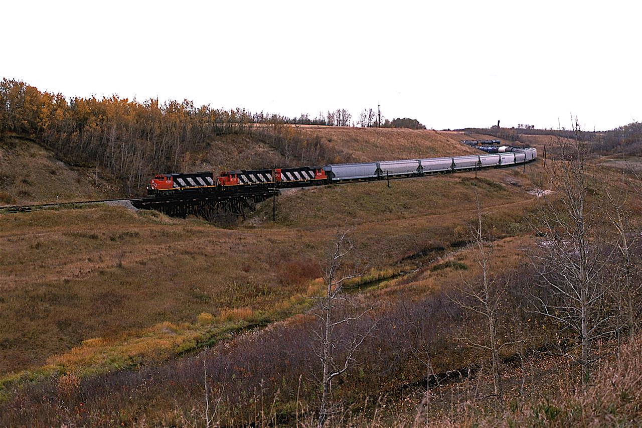 In spite of the miserable clouds, I shot the 550 as it worked further down the Camrose creek valley. This train will work Mirror, and then head out the Brazeau sub, when it will service the industries out that way and switch Red Deer.
The engines are on the 4th of nine wooden trestles in this small valley. The train is on the 3rd trestle, but it is in the hidden part of the train.