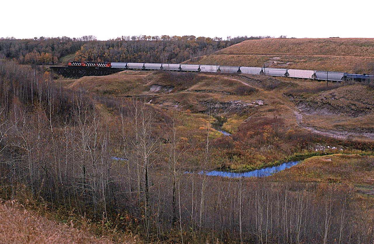 Another view of 550 as it continues down Camrose Creek Valley. The treatle that the train is occupying is no more. It is now an earthen berm. 
Those hoppers are probably going to the polyethylene plant a Joffre AB.