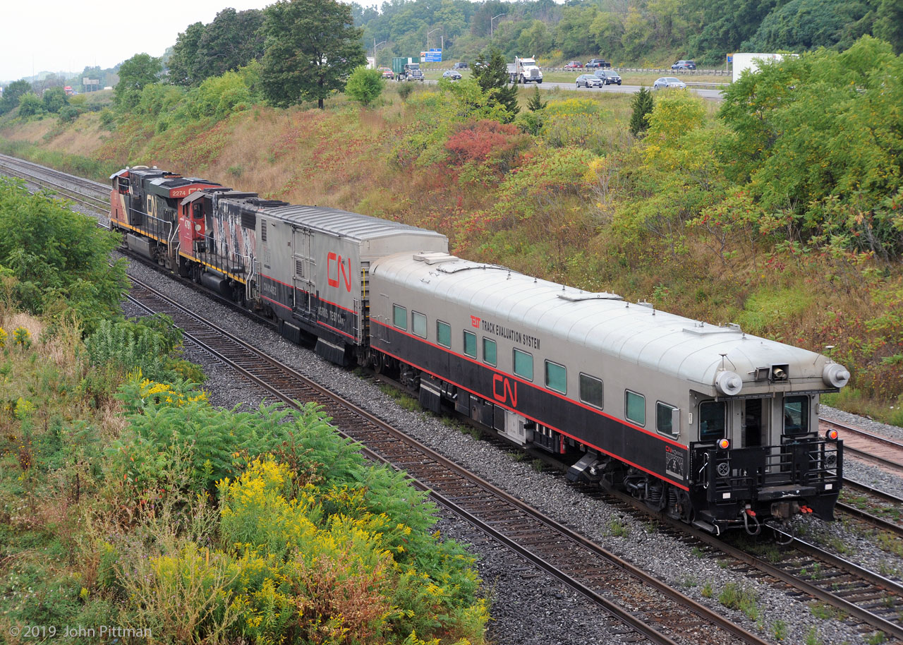 A CN TEST Track Evaluation System train was proceeding west on the Oakville Sub, beyond Aldershot Yard at 9:11 EDT on "9/11".
It was heading to Hamilton and the Grimsby Sub. Odd that the mp33 detector reported 19 axles. 
The lead engine, ES44dc CN 2274 had a rectangular box on its front hood (resembling an outdoor security camera) and a dashcam-like device inside the left cab window.
The modified boxcar is CN 414852 "DGRMS Test Car". The TEST Track Evaluation System coach is CN 1057. 
Both have CN Engineering emblems.