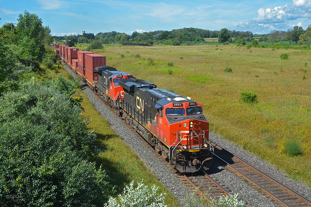 Canadian National Railway intermodal train Q 10851 passes through Newtonville, Ontario, on August 25, 2019.  CN ES44AC 2893 and Dash 8-40CW 2144 (ex-BNSF 818, nee-ATSF 818) are pulling this 10,237-foot train of 135 loads and 20 empties, weighing 8,754 tons, as it makes its way from Vancouver BC to the eastern part of Canada.