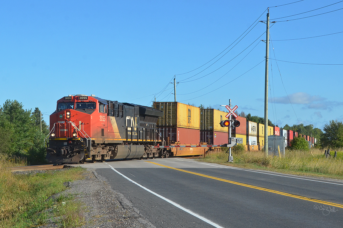 Southbound Canadian National train Q 11251, an intermodal train, passes through Georgina, in Ontario's York District, on August 30, 2019.  This train's journey began about 2775 miles (4466 km) to the west, in Vancouver, British Columbia, and will be over soon as it is only around 55 miles (88 km) away from its final destination of Toronto, Ontario.  CN ET44AC 3055 is up front, with CN ES44AC 3803 helping out in the middle of the train.