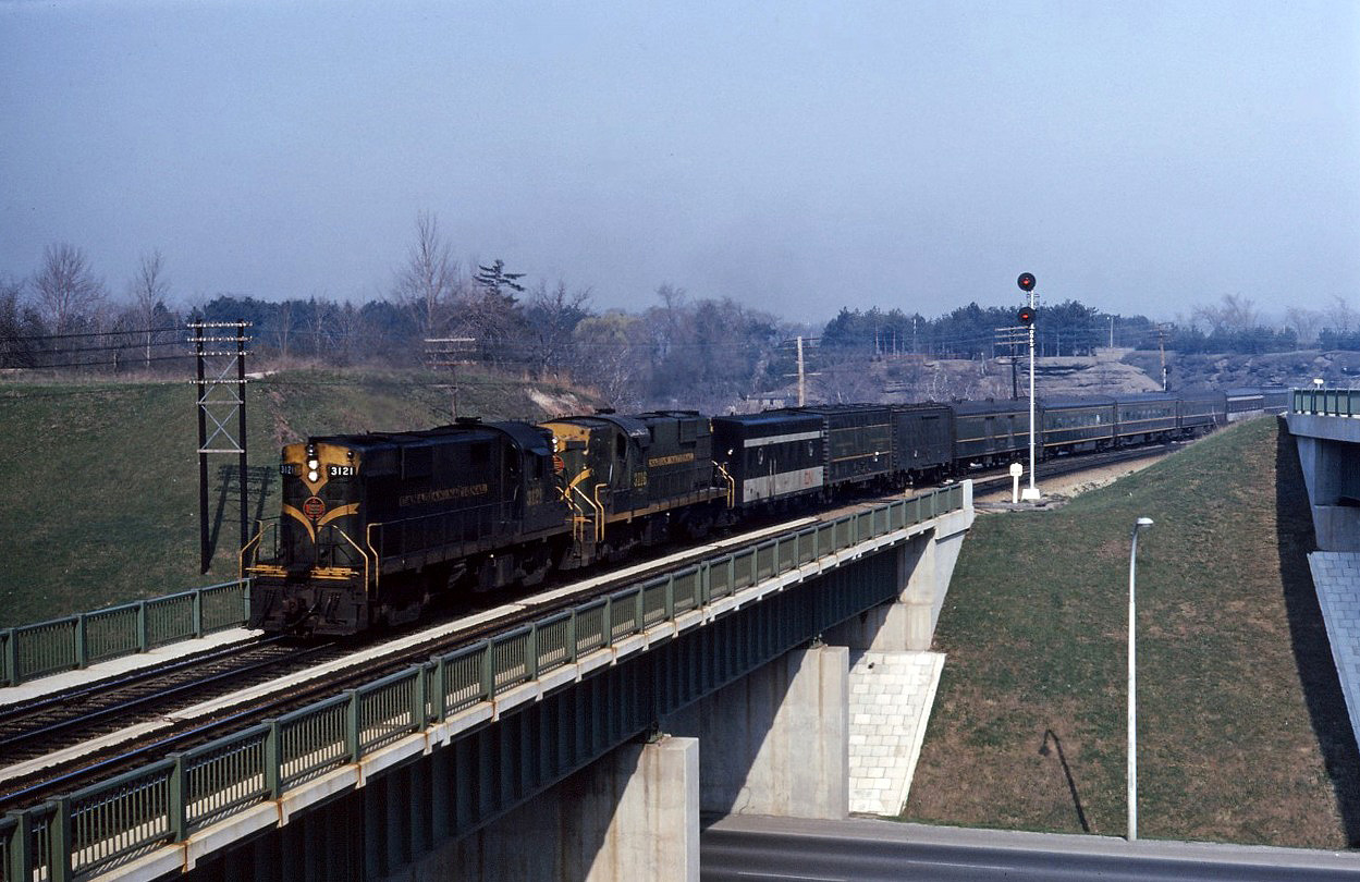 RS18s 3121 and 3116 lead an interesting consist on Toronto-Windsor train No. 75 in the spring of '65. Note the head end cars: an SGU, two express refrigerators, a baggage car plus three different types of coaches (mostly green/black but the "new" CN images is starting to appear). Also note the "Begin CTC" sign next to the high mast signal 006S (which has additional height to improve signal sighting for approaching trains).