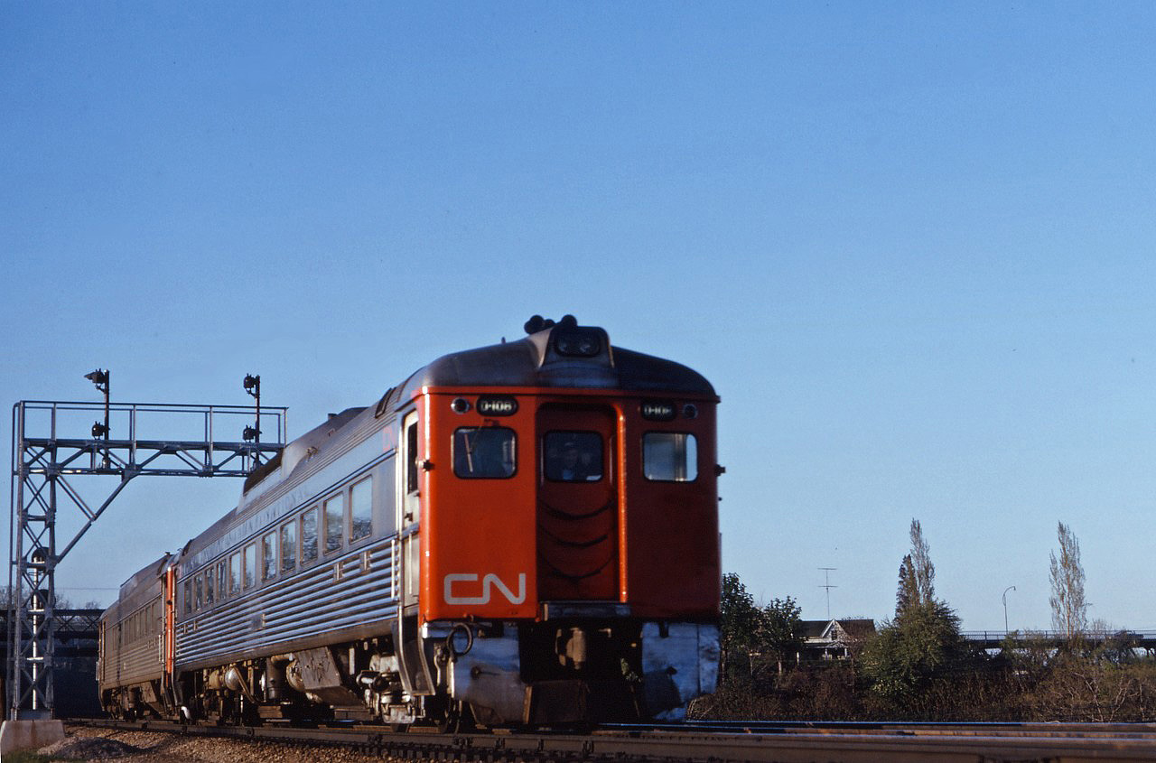 On a fine early summer evening, the "dinner time" train for Niagara Falls rolls through Bayview with two "Budd cars" sporting the new image. However, if you look closely, you can still see "Canadian National" lettering above the windows and will notice that there is no black stripe typical of later repaints. (Several RDCs remained in this variant of the paint scheme into the mid-1970s.)

Also of interest is the new signal cantilever being installed with Centralized Traffic Control over to Burlington and up the Halton sub to the new Toronto Yard. (The 1957 CTC installation only controlled Bayview, Hamilton Jct, Hamilton West, Hamilton Yard and N&NW Jct.)