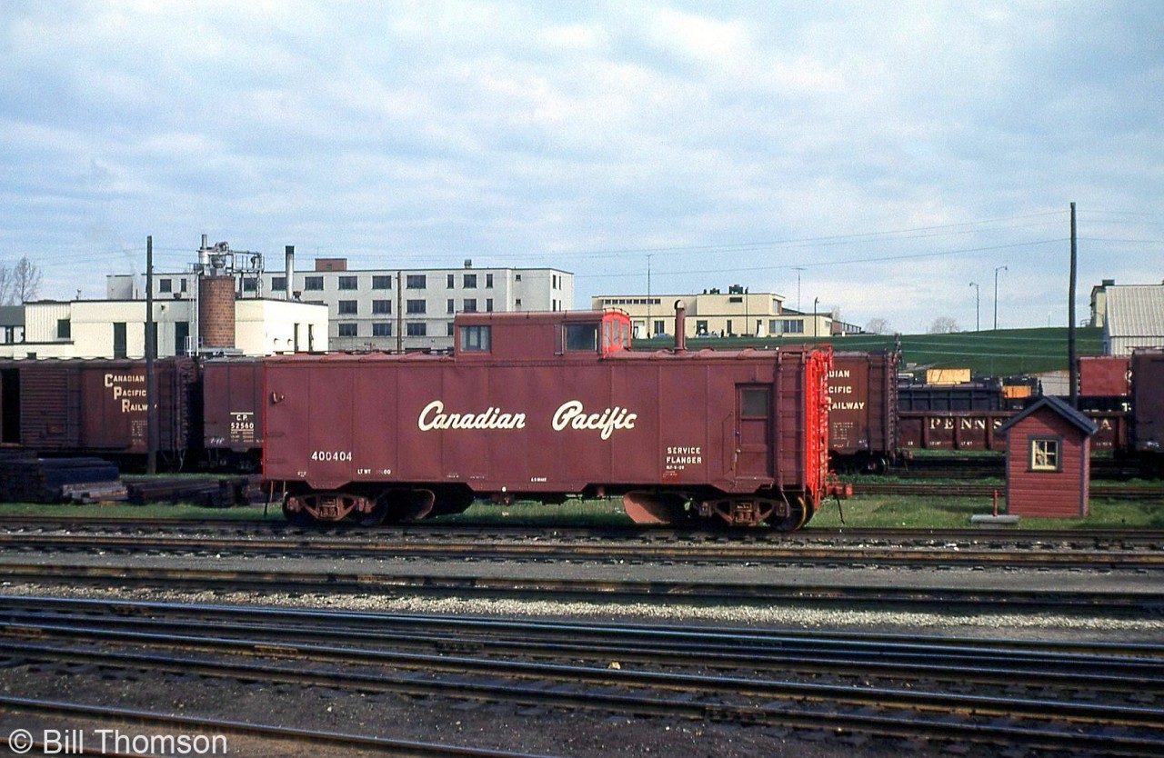 Canadian Pacific flanger 400404 is seen amid other freight equipment in the yard in London in 1966. Like CN, CP also had their own flanger cars stationed around the system for clearing snow and ice from the flangeways between rails.

Like many other flangers CP had, this car had been converted from one of CP's fleet of steel "minibox" boxcars originally built in 1929/1930 (that were shorter in height than most regular steel boxcars). As newer larger boxcars displaced them, many miniboxes migrated into maintenance of way service, including becoming tool cars, bunk cars, flangers, and generator cars. On this car, twin flanger blades have been mounted behind each of the trucks, a cupola added to the roof, access doors cut into the sides, and the old center 5' sliding door has been removed and opening covered over to match the rest of the body.