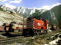 MLW yard 7115, CLC C-Liner 4053 and a Geep sit on the servicing area at the Summit of Crowsnest Pass. Mount Ptolemy forms the backdrop