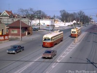 TTC PCC 4550 (an A9-class car originally built for Cincinnati in 1947) passes A8-class PCC 4542, both operating on the mid-town St. Clair route on St. Clair Avenue West at Caledonia Road. 4550 is about to pass under Canadian National's Newmarket Sub near the CN St. Clair Ave station, whose platform extended south over the bridge. Note the ever-present Milnes Coal & Fuel dealer on the left (who themselves had a rail siding) and the typical assortment of 60's automobiles including Ford Mustangs and VW Bugs.<br><br>The Newmarket Sub used to cross St. Clair Avenue at-grade where the streetcars are pictured, and streetcars on St. Clair terminated at loops on either side of the CN tracks (requiring an on-foot transfer between Dovercourt cars to the west and St. Clair cars to the east). A grade separation project undertaken in the late 1920's/early 1930's resulted in a new overpass constructed at St. Clair to allow St. Clair streetcars to travel further west, as well as a new <a href=http://www.railpictures.ca/?attachment_id=34053><b>CN St. Clair Avenue station</b></a> (to the left out of frame) that replaced the old Davenport Station further south. Much of the old rail line alignment became a lead to local spurs and sidings to serve customers to the south of St. Clair, notably numerous Italian wine and produce suppliers like Darrigo Brothers, Pietro Culotta, the Meschino Banana Company, and Caledonia Food Distributors (A&P also had a rail-served warehouse nearby).<br><br><i>Original photographer unknown, Dan Dell'Unto collection slide.</i>
