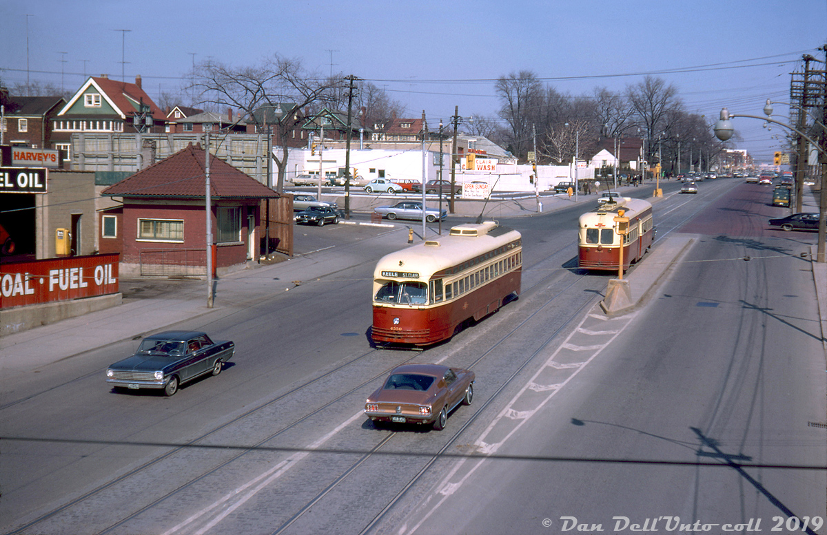 TTC PCC 4550 (an A9-class car originally built for Cincinnati in 1947) passes A8-class PCC 4542, both operating on the mid-town St. Clair route on St. Clair Avenue West at Caledonia Road. 4550 is about to pass under Canadian National's Newmarket Sub near the CN St. Clair Ave station, whose platform extended south over the bridge. Note the ever-present Milnes Coal & Fuel dealer on the left (who themselves had a rail siding) and the typical assortment of 60's automobiles including Ford Mustangs and VW Bugs.The Newmarket Sub used to cross St. Clair Avenue at-grade where the streetcars are pictured, and streetcars on St. Clair terminated at loops on either side of the CN tracks (requiring an on-foot transfer between Dovercourt cars to the west and St. Clair cars to the east). A grade separation project undertaken in the late 1920's/early 1930's resulted in a new overpass constructed at St. Clair to allow St. Clair streetcars to travel further west, as well as a new CN St. Clair Avenue station (to the left out of frame) that replaced the old Davenport Station further south. Much of the old rail line alignment became a lead to local spurs and sidings to serve customers to the south of St. Clair, notably numerous Italian wine and produce suppliers like Darrigo Brothers, Pietro Culotta, the Meschino Banana Company, and Caledonia Food Distributors (A&P also had a rail-served warehouse nearby).Original photographer unknown, Dan Dell'Unto collection slide.