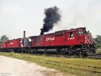 Dark smoke erupts from MLW M630 CP 4566, which could be due to a sudden throttle advance or engine restart.<br> Apparently the diesel engines of the other units are running better/cleaner. In other images taken at same place same day, CP 4566 did not have visible smoke.<br><br>
The engines are at the east end of CP Quebec Street Yard just east of the namesake overpass, leading an eastbound train.<br>
The trailing unit has been modified by addition of numerous car body air filters; its appearance matches M636 CP 4716 in this timeframe. 