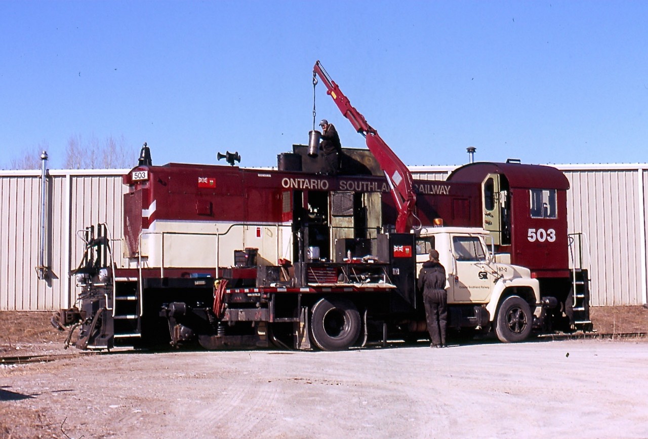On this date the new OSR shop in Guelph Jct was still new and lacked lighting and a pit so most maintenance of locomotives was still done outside. In this case the workers needed a small crane as it appears OSRX 503 was having a cylinder changed out.