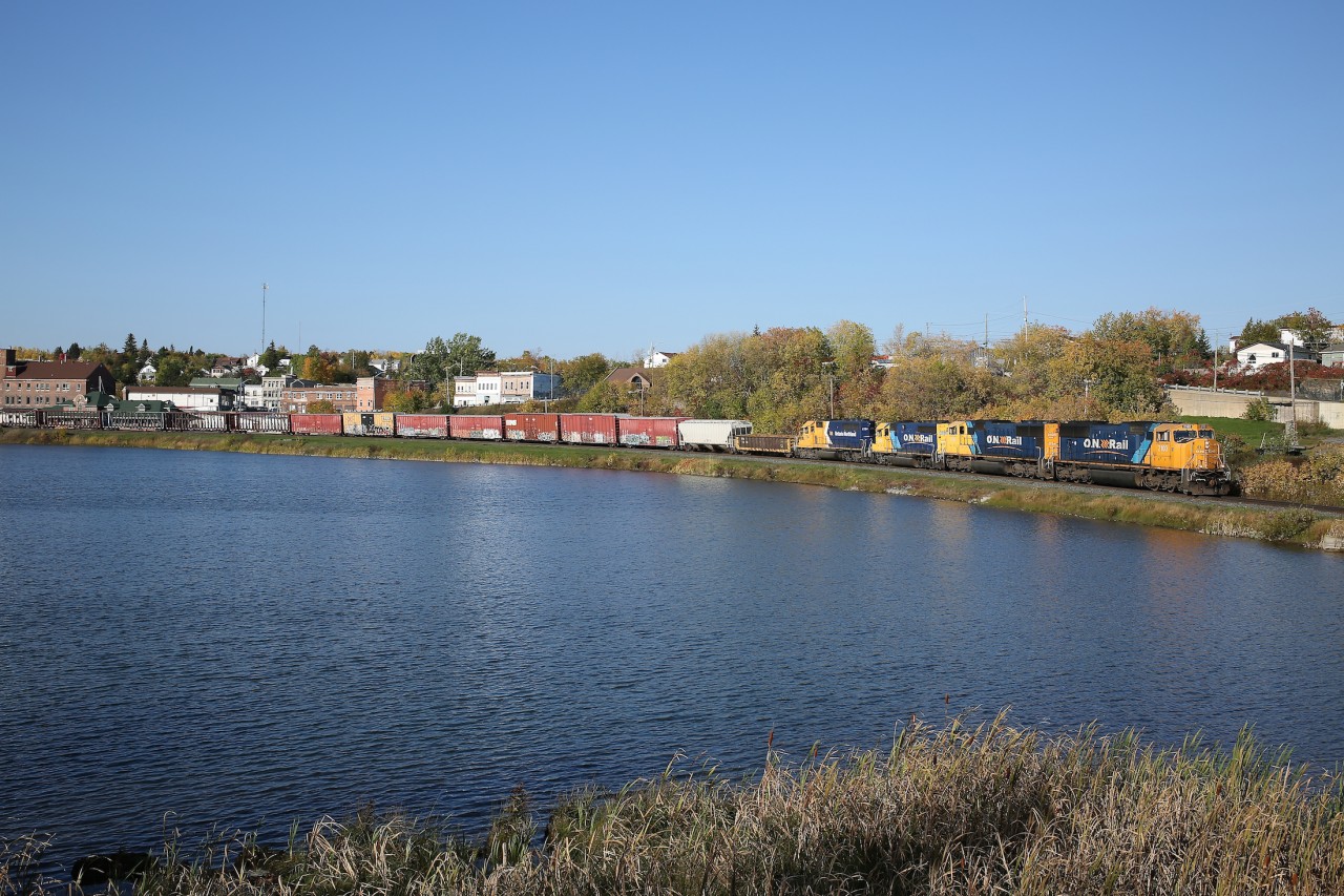 A quartet of Ontario Northland engines lead train 113 along the shoreline of Cobalt Lake.  To the left, partially hidden by some empty centrebeam cars, is the town's historic train station.