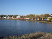 A quartet of Ontario Northland engines lead train 113 along the shoreline of Cobalt Lake.  To the left, partially hidden by some empty centrebeam cars, is the town's historic train station.