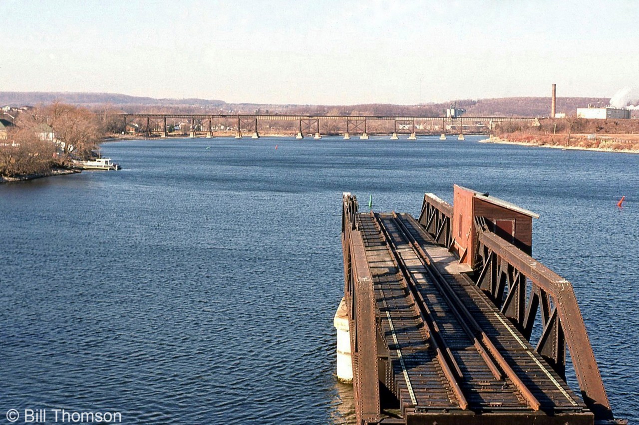 The old Canadian Northern (CNoR) swing bridge over the Trent River in Trenton is pictured in the foreground, swung in the "open" position. In the background is CP's long trestle for their Belleville Sub. At the time, the line crossing the old CNoR bridge was a CN spur track branching off CN's Trenton Spur (former Maynooth/Marmora Sub) and still in use to access industries on the east side of the river. Today, both the line and bridge spans have since been removed, leaving only the abutments.