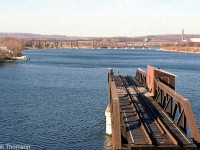 The old Canadian Northern (CNoR) swing bridge over the Trent River in Trenton is pictured in the foreground, swung in the "open" position. In the background is CP's long trestle for their Belleville Sub. At the time, the line crossing the old CNoR bridge was a CN spur track branching off CN's Trenton Spur (former Maynooth/Marmora Sub) and still in use to access industries on the east side of the river. Today, both the line and bridge spans have since been removed, leaving only the abutments.